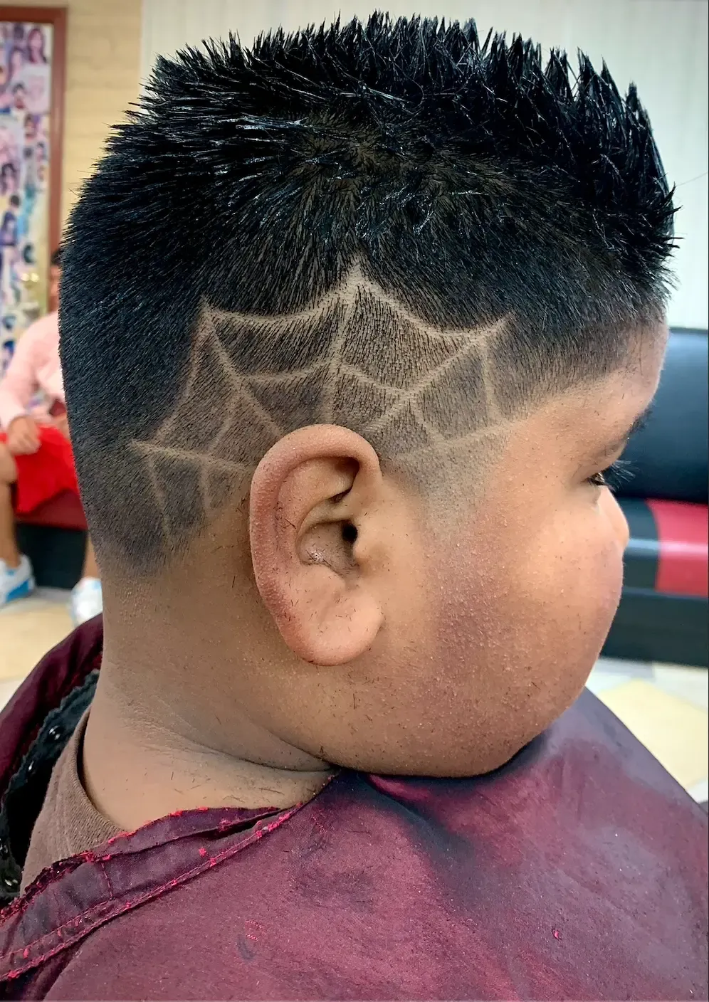 Side of a boy's head with a spider-web design shaved into a fade and a spiky top