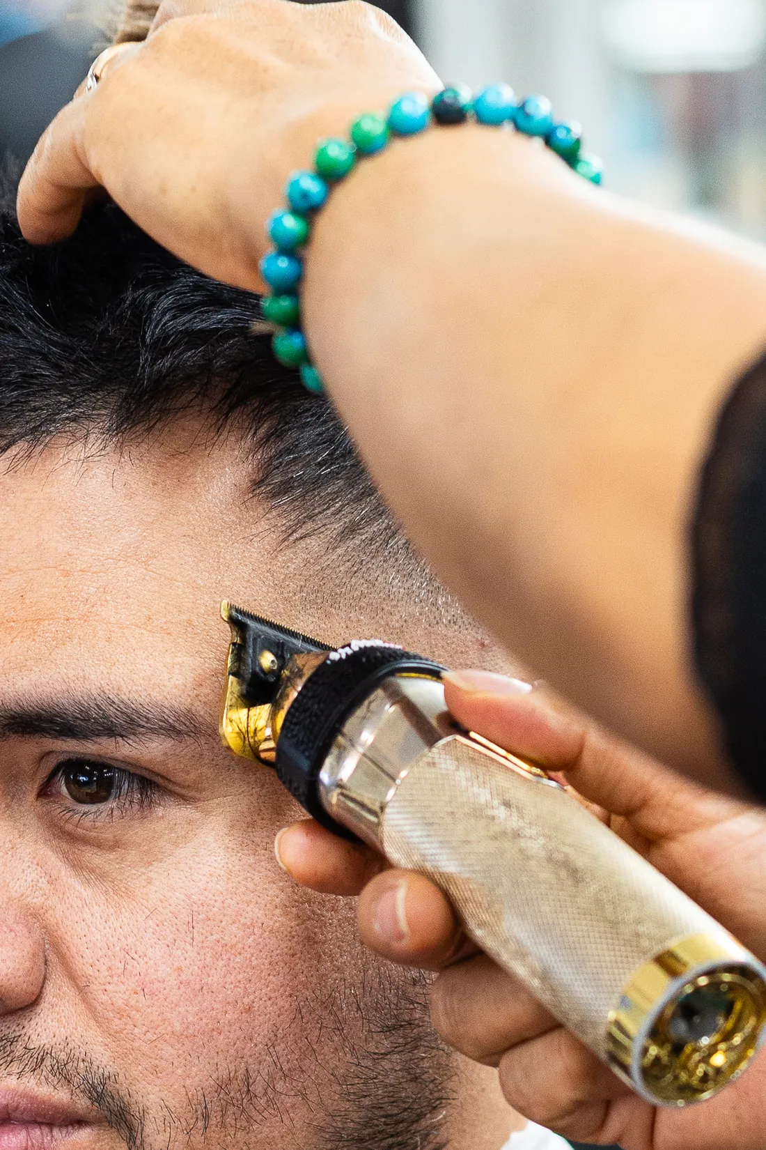 Close-up of a barber using a gold trimmer to line up a client's hairline at the temple