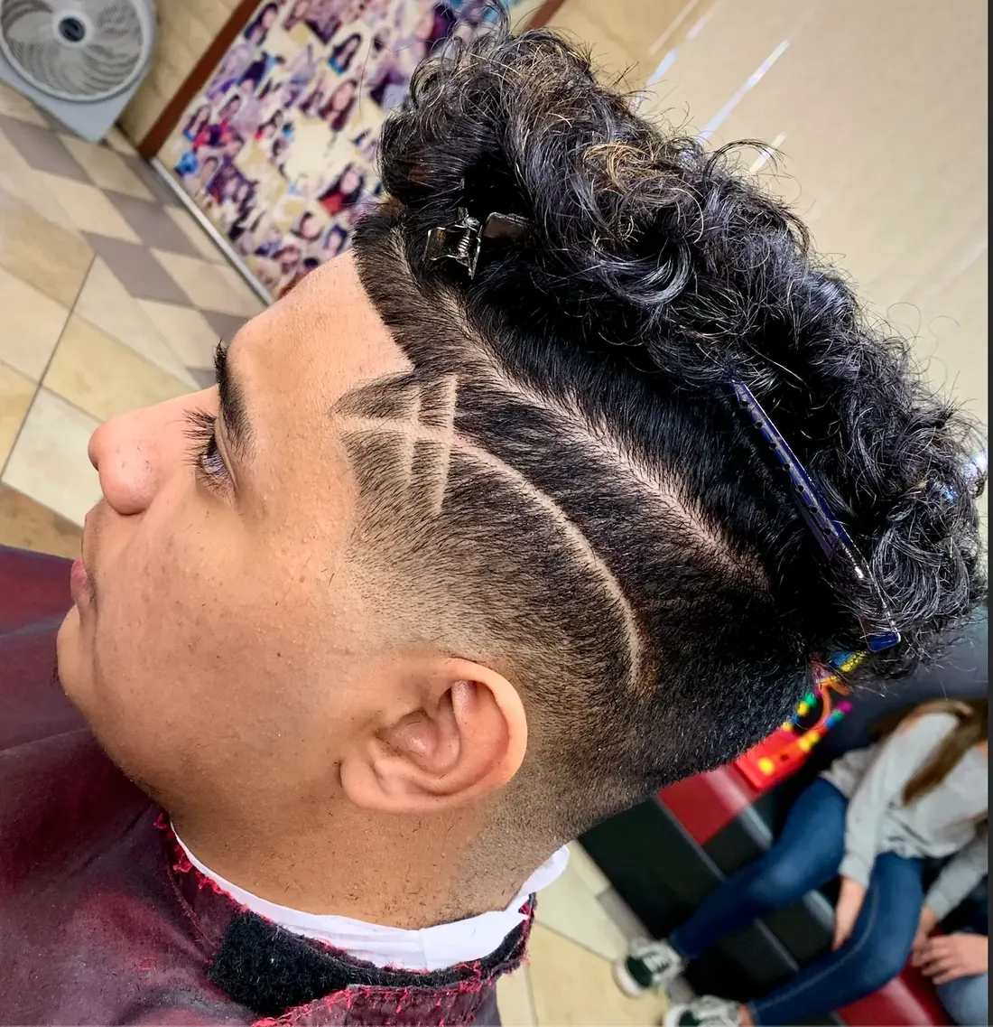 Client with curly hair on top and a taper with several shaved line designs on the side