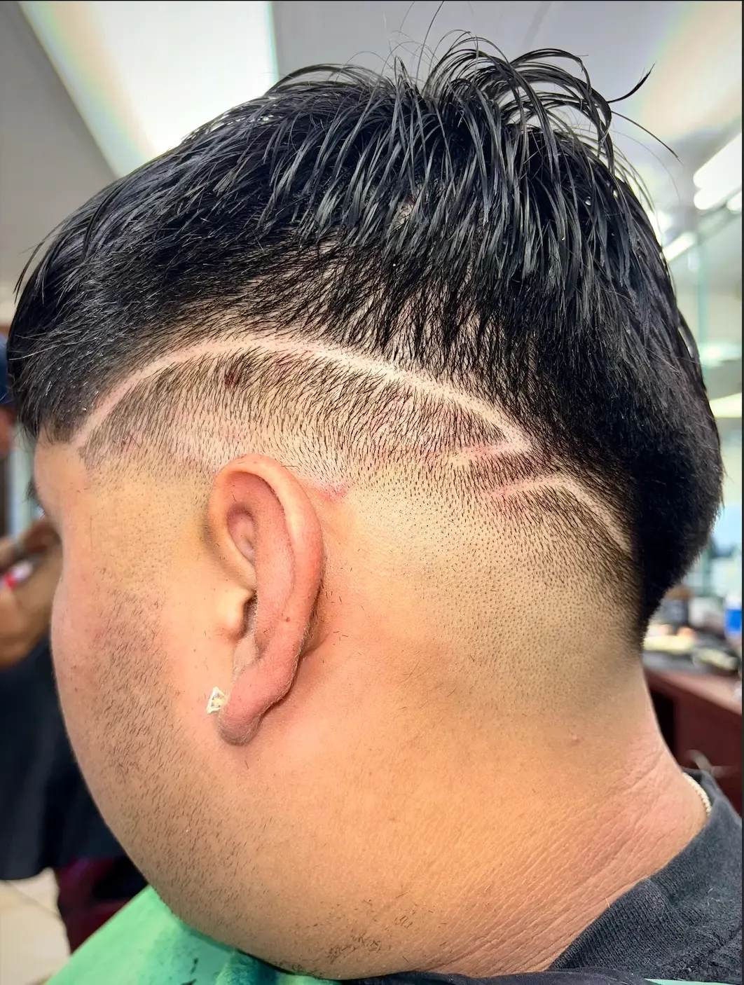 Back-side view of a skin fade with a long curved line design running above the ear