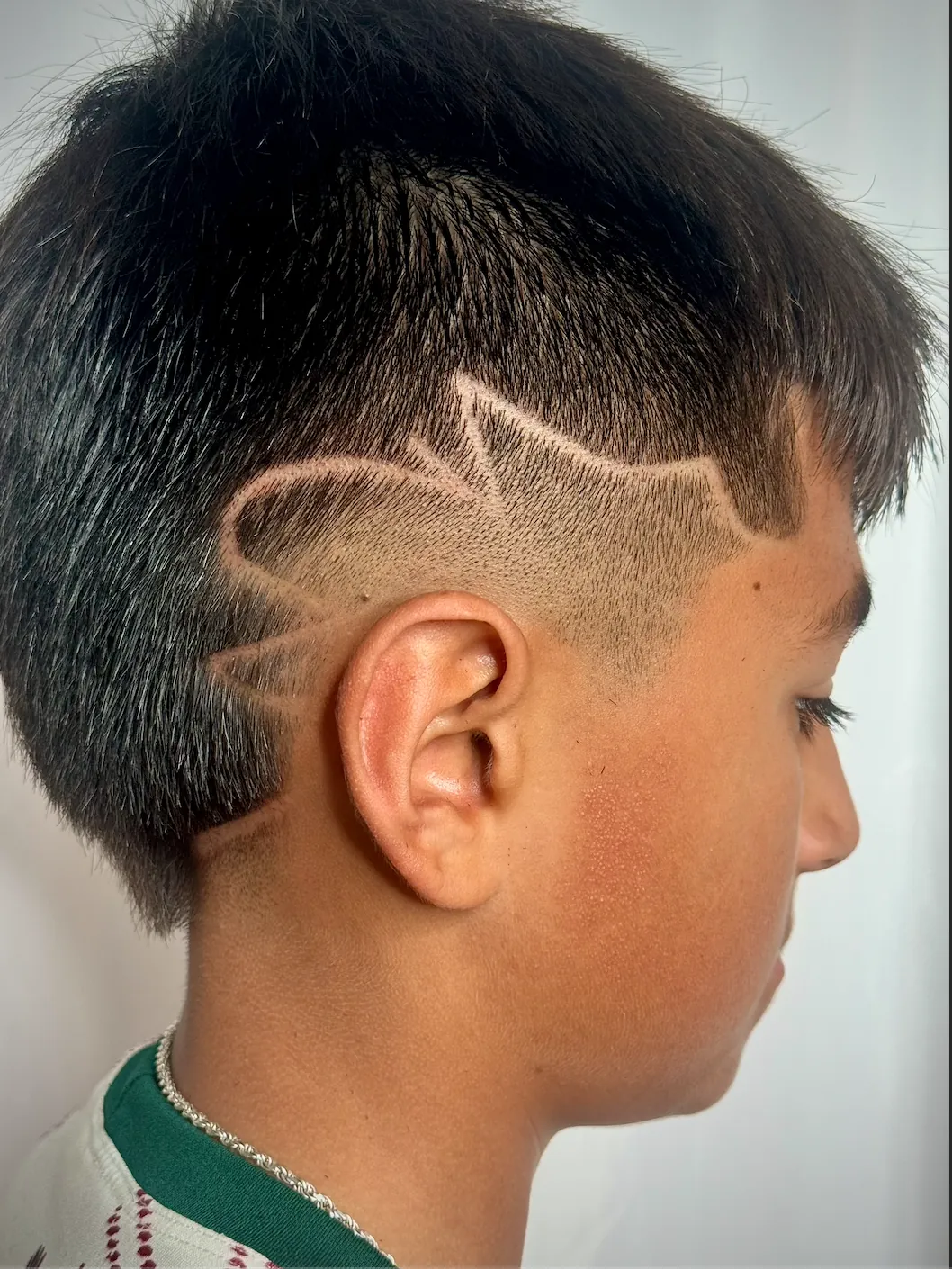 Side profile of a boy with a fade and a lightning-style line design above the ear