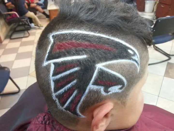 A football team falcon logo shaved and colored in red, black and white into the side of a client's head