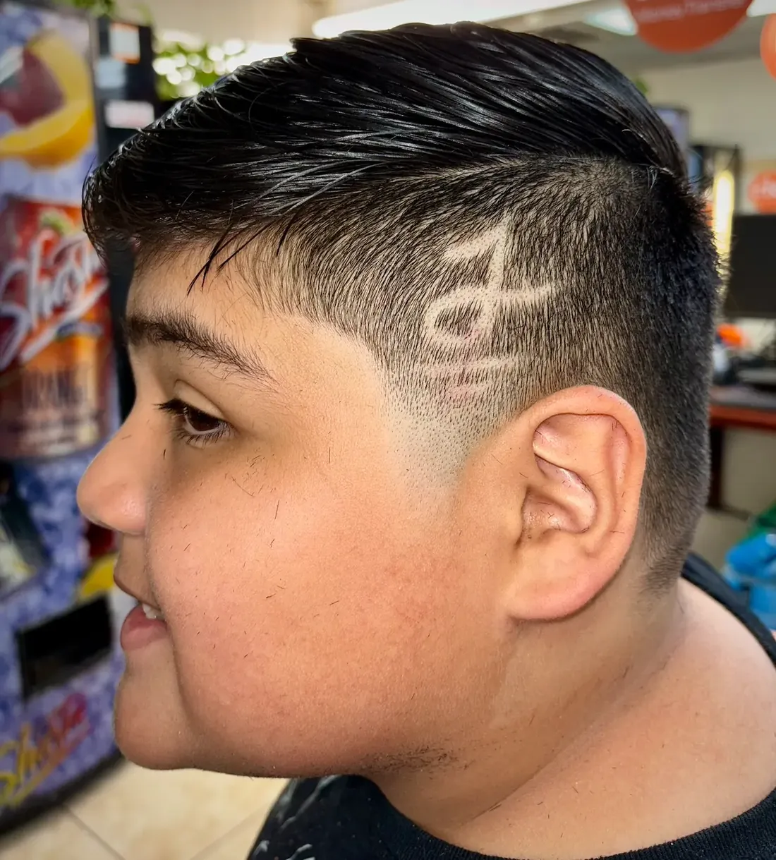 Smiling boy with a swept top and a freehand design shaved into the side of his fade