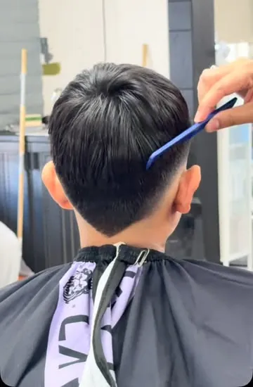 Back view of a boy's fresh taper haircut while the barber combs the top