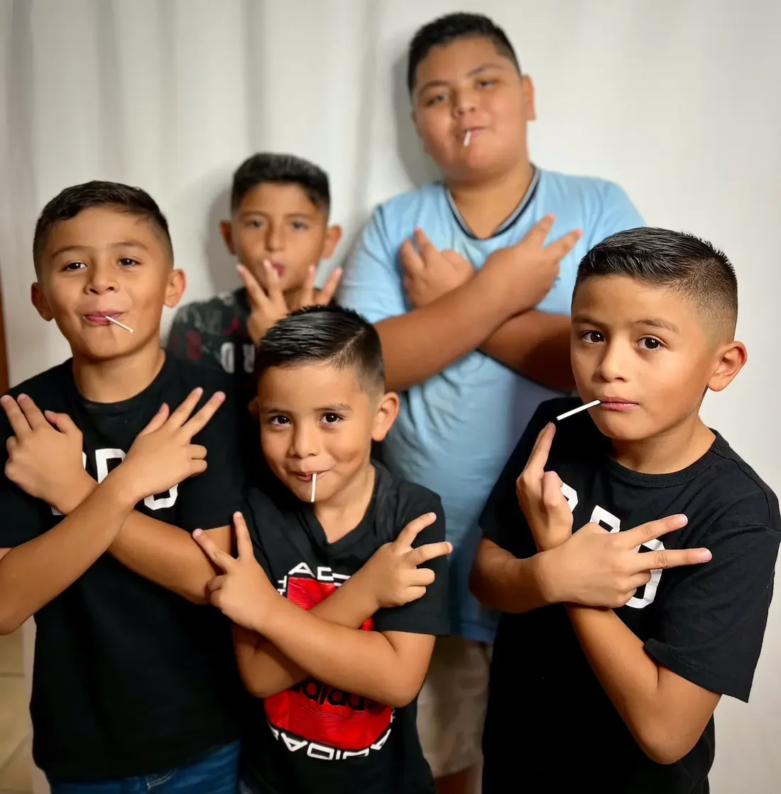 Five boys with fresh haircuts posing together with arms crossed and lollipops