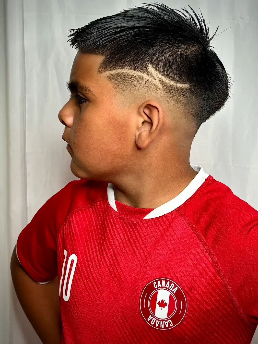 Boy in a red soccer jersey showing a fade with a curved line design on the side