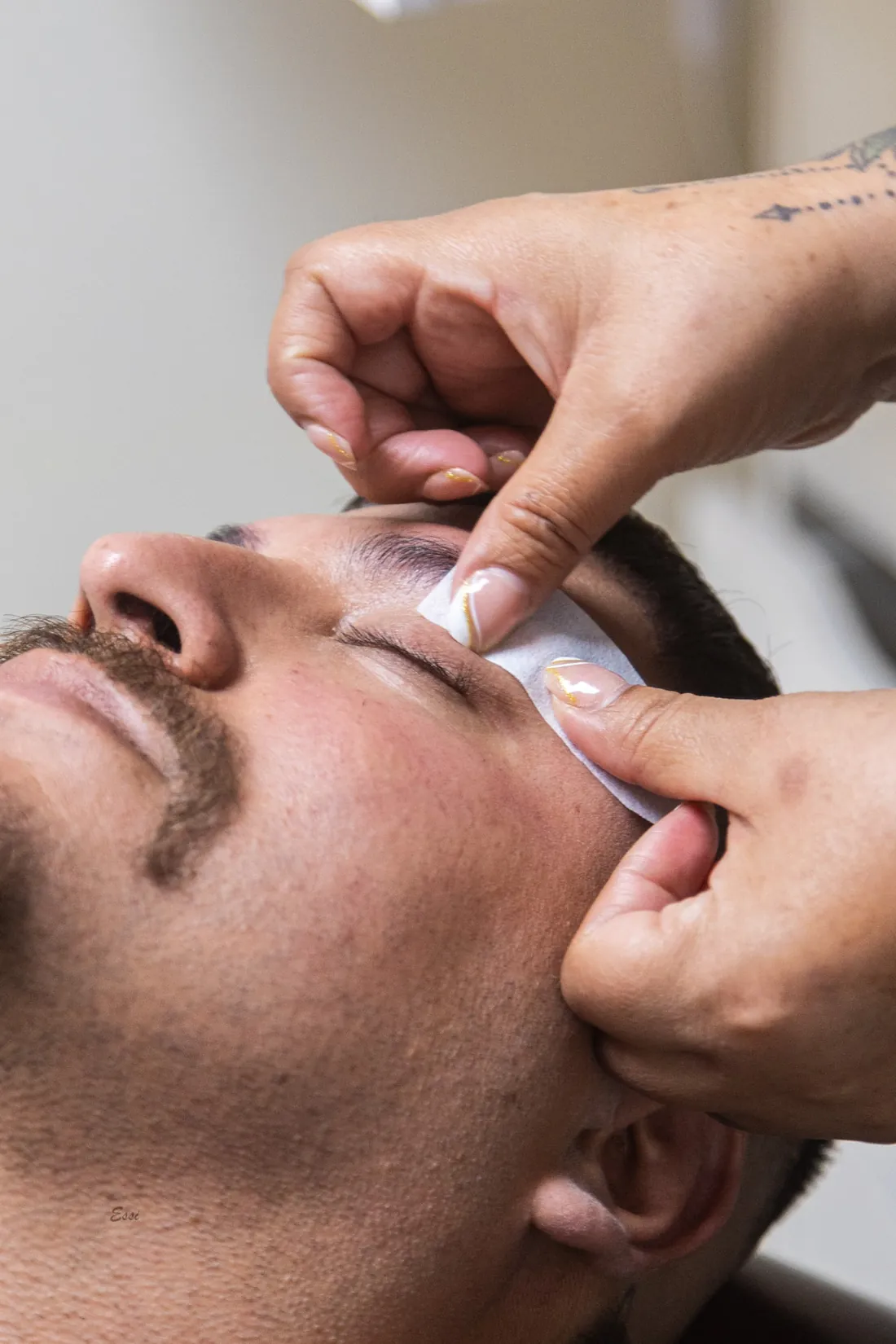 Close-up of hands pressing a wax strip along a client's eyebrow