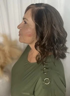 Side profile of a woman with shoulder-length dark hair styled in soft curls with subtle lighter tones