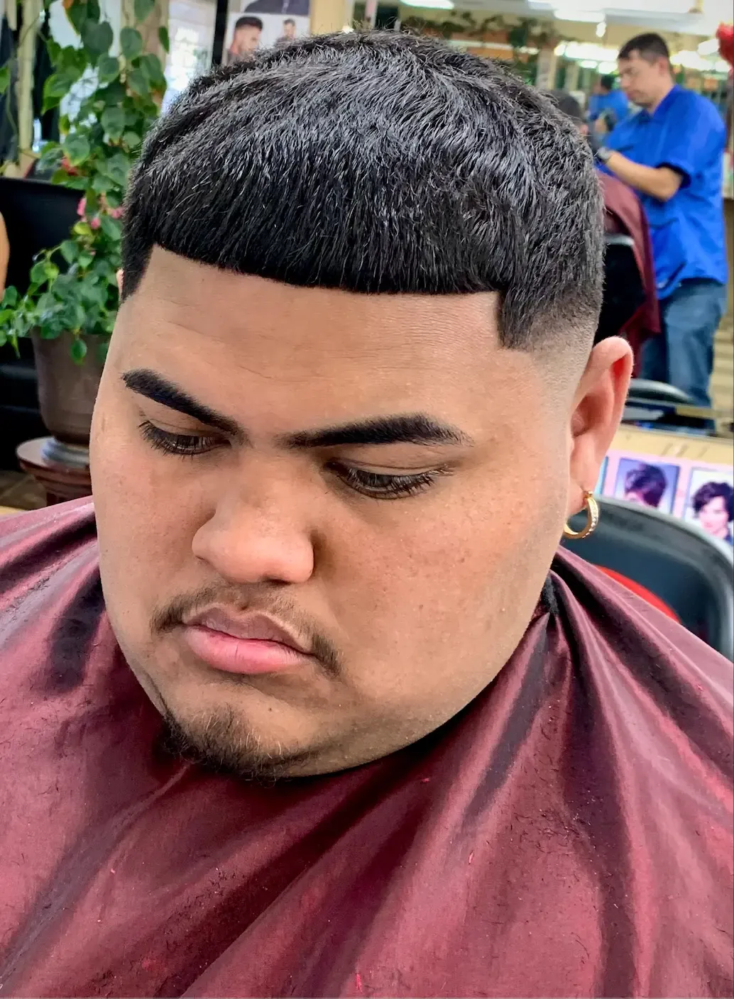 Young man in a burgundy cape with a textured crop, straight fringe and low fade, inside the shop